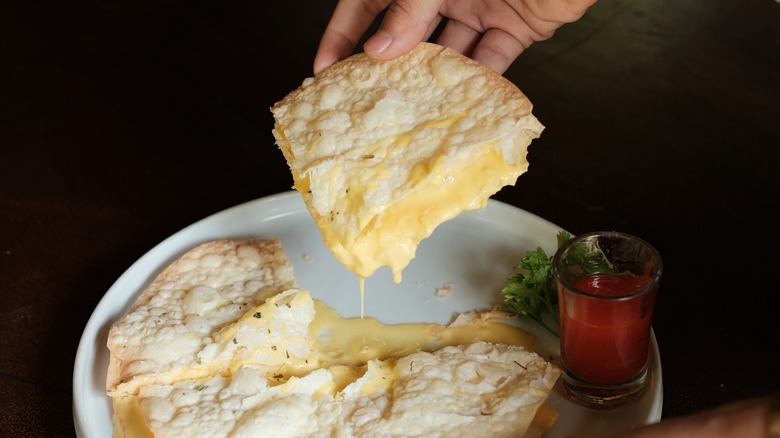 Hand picking up a slice of an extra cheesy quesadilla