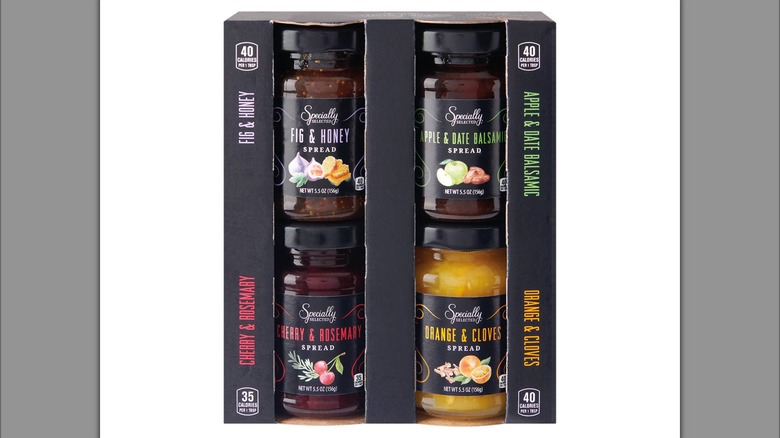 A cardboard box holding four jars of different flavored fruit spreads