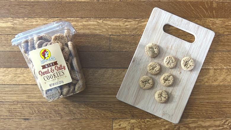 Plastic container of and handful of Buc-ee's Mini Sweet & Salty Cookies on a wooden cutting board