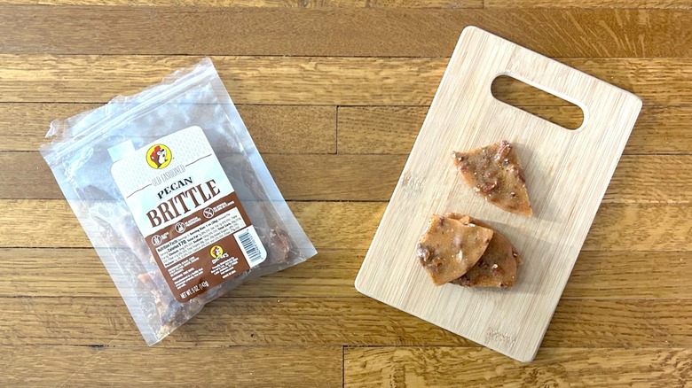 Package of and handful of pieces of Buc-ee's Pecan Brittle on a wooden cutting board