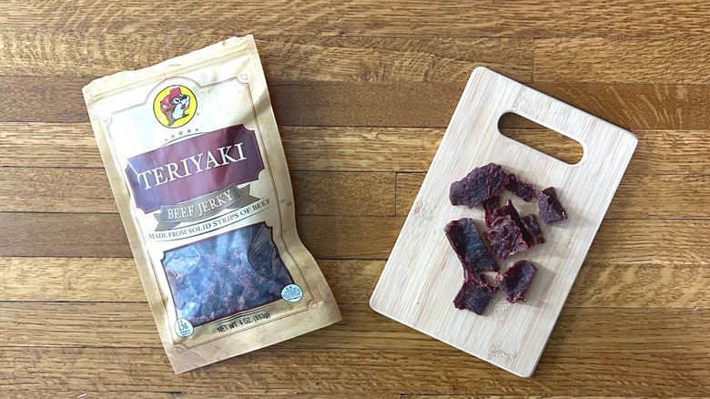 Package of and handful of Buc-ee's Teriyaki Beef Jerky on a wooden cutting board