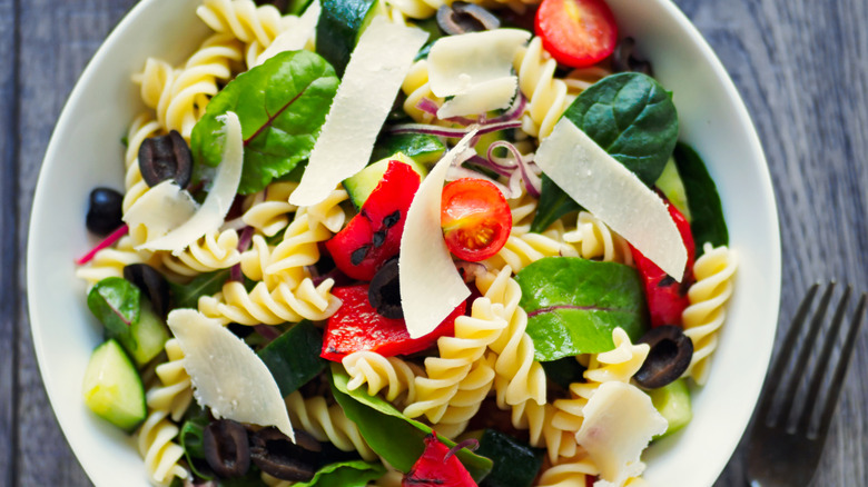 Bowl of pasta salad with fresh veggies, shaved cheese, and black olives