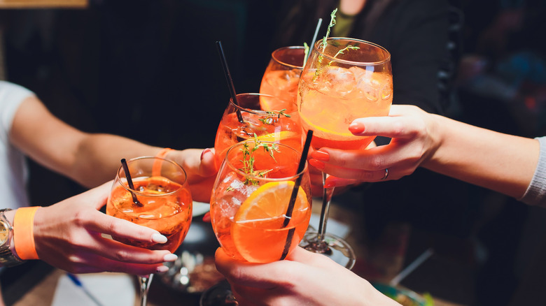 Hands clinking wine glasses filled with Aperol Spritz