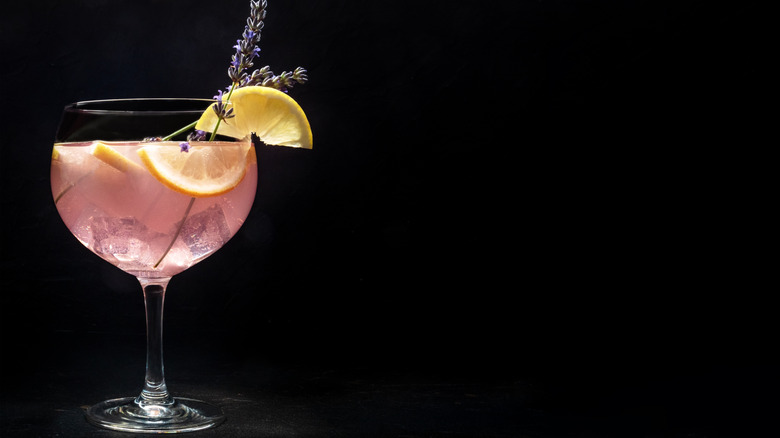 Pink cocktail in wine glass garnished with lemon and lavender