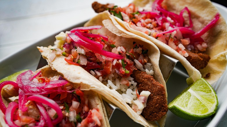 Line of fish tacos with red onions on top