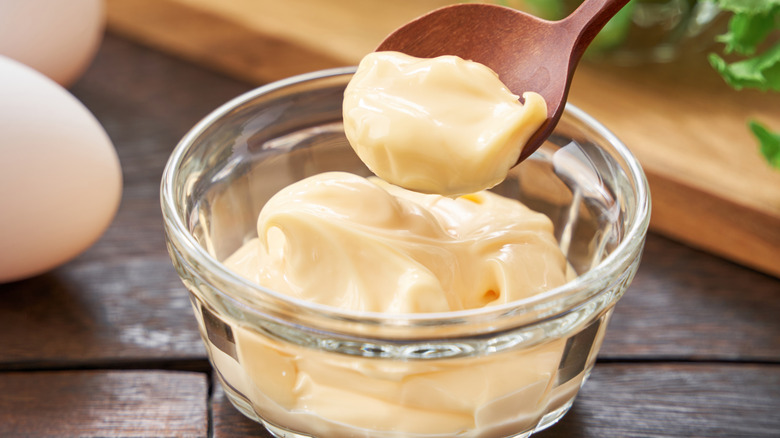 Wooden spoon scooping mayo out of clear bowl