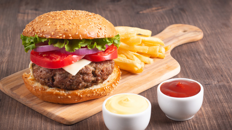 Burger on wooden cutting board beside condiments