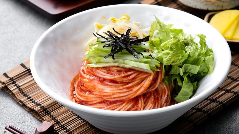 A bowl of bibim guksu topped with green onions and lettuce