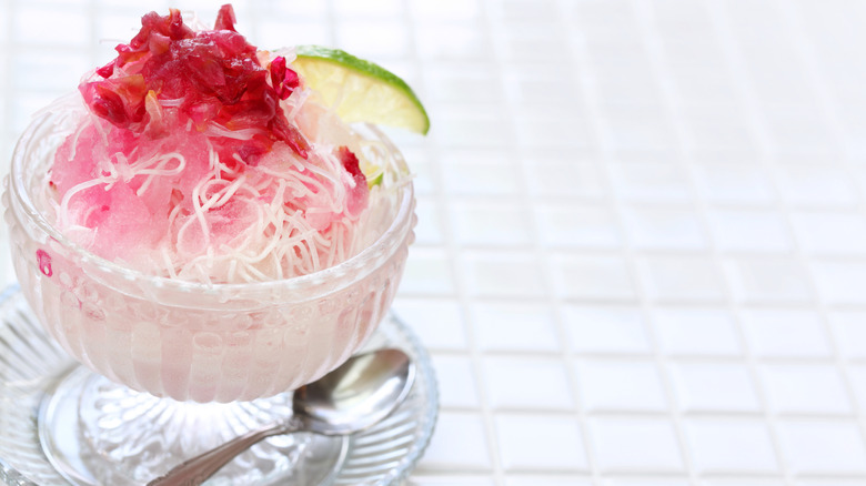 A glass dish of faloodeh topped with chopped cherries and a lime wedge