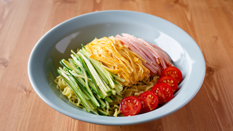 A bowl of hiyashi chuka with sliced cucumber, omelet, ham, and cherry tomatoes