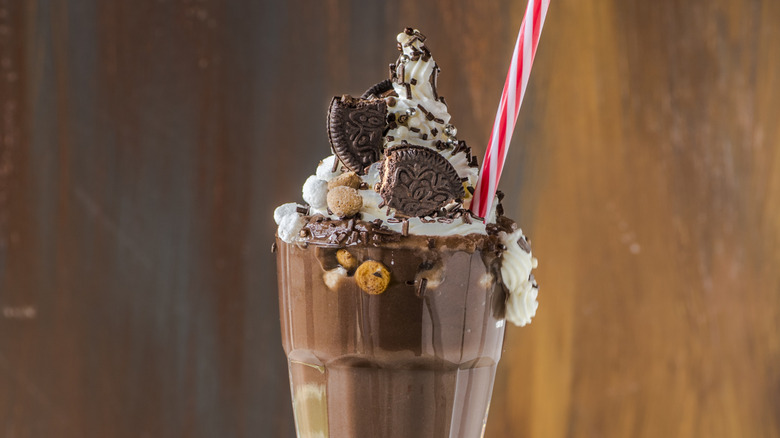 A chocolate milkshake with a straw, cookies, and whipped cream