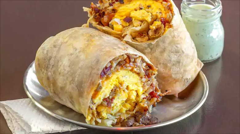 A burrito with soujouk inside of it on a yellow background with green sauces beside it.