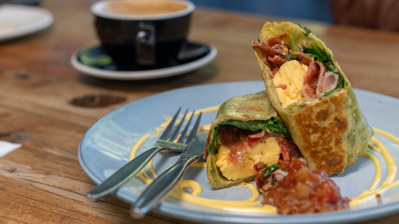 A breakfast burrito on a plate beside a cup of coffee