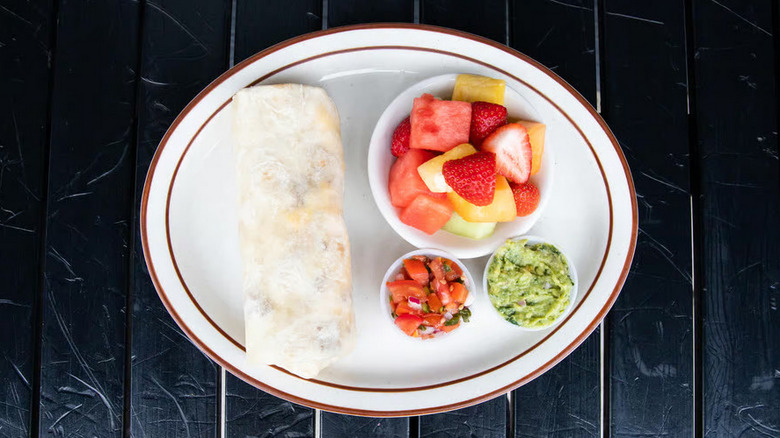 Breakfast burrito on a plate with guacamole, fruit, and salsa