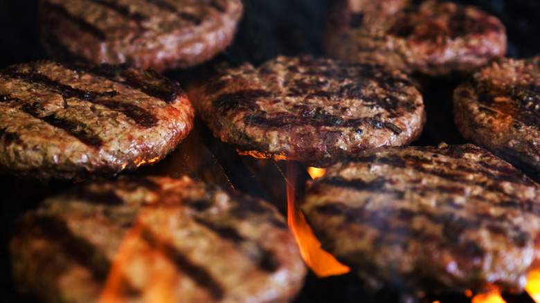 Burgers grilling with flames under the grill grates