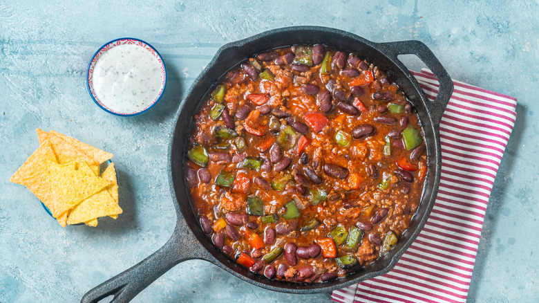 A pan of chili with chips and a creamy dip on the side