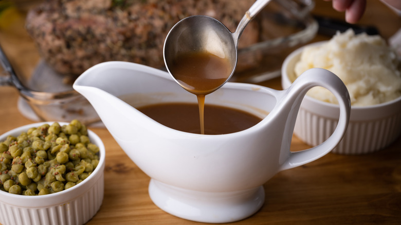 A gravy boat with a spoon, peas, and mashed potatoes