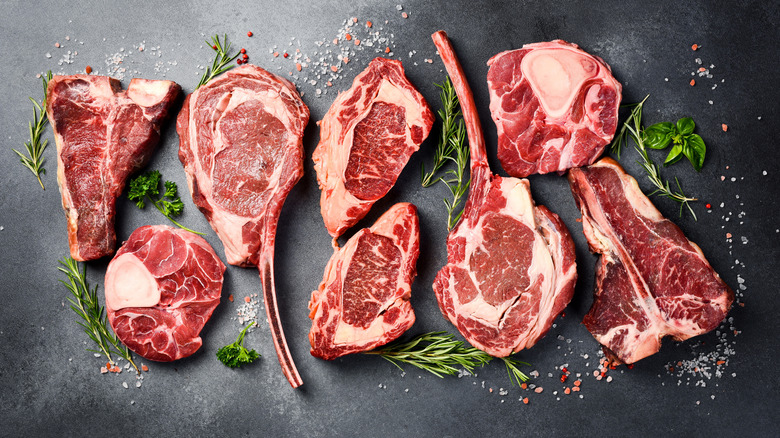 Raw steaks on a gray surface with herbs