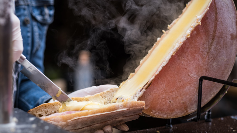 A person scraping raclette cheese into a baguette