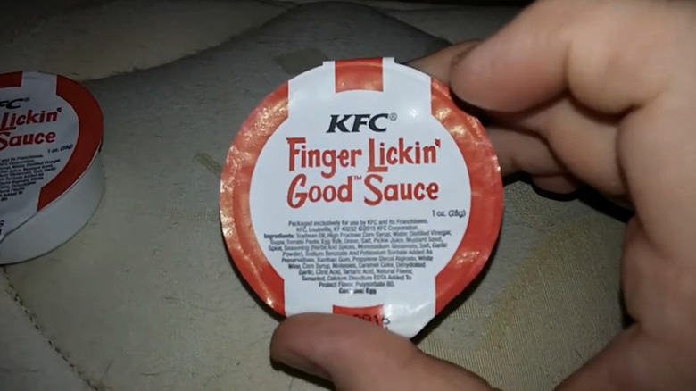 Someone holding a small container of KFC Finger Lickin' Good Sauce