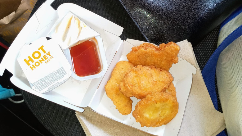 A takeout box of chicken nuggets with an open packet and a closed packet of hot honey sauce