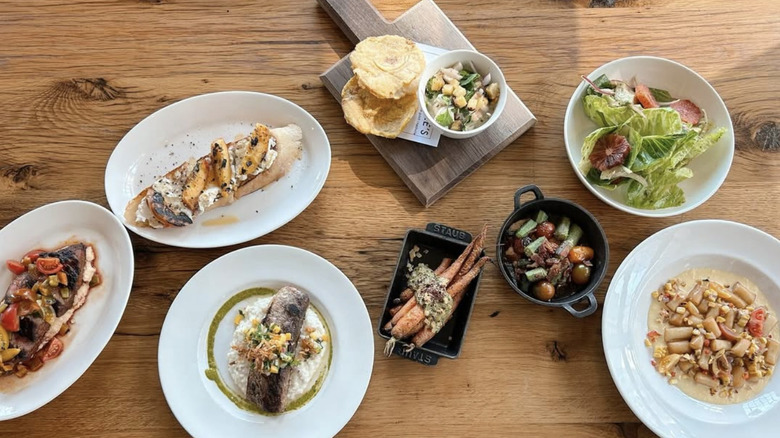 Plates of food on a wooden table, including fish dishes and salads