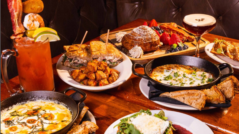 A decadent brunch spread, including egg shakshuka, a club sandwich and patatas bravas, brioche with berries, a Bloody Mary garnished with shrimp and bacon, and an espresso martini