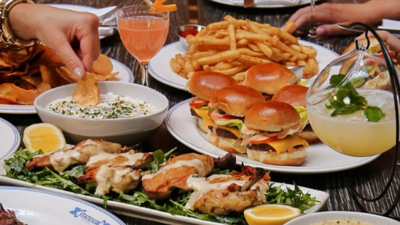 A brunch spread of sliders, chicken wings, and chips and dip, with cocktails