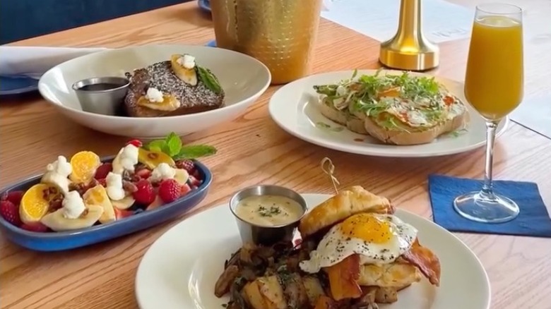Brunch plates loaded with fresh fruit, avocado toast, steak, and more, alongside a mimosa in a champagne flute