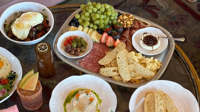 Brunch dishes and a brunch platter loaded with fresh fruit, bread, and charcuterie set out on a glass table