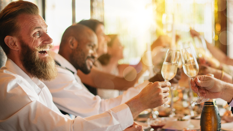 smiling people making toast at dinner party