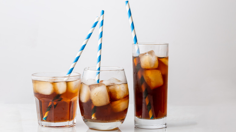 Three glasses of dark soda with ice and striped straws