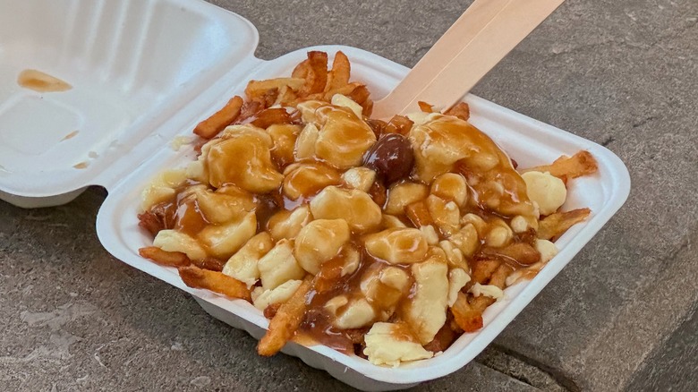 An open to-go box of poutine with a wooden fork
