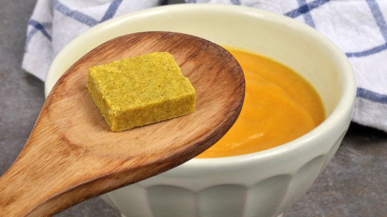 cube broth in a wooden spoon over a bowl