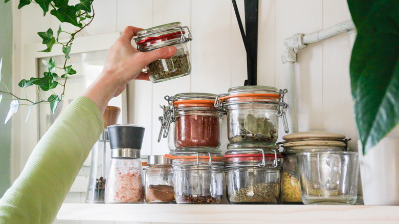 a hand reaching for a jar among a collection of spices
