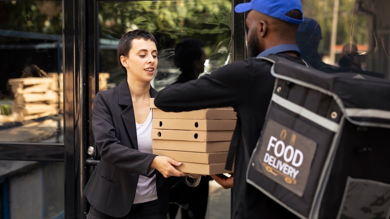 Man delivering large stack of pizza boxes to woman