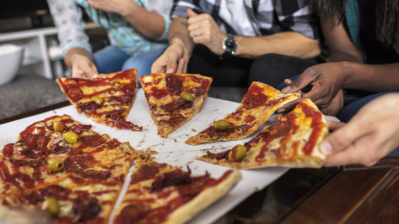 Group of friends pulling slices from pizza