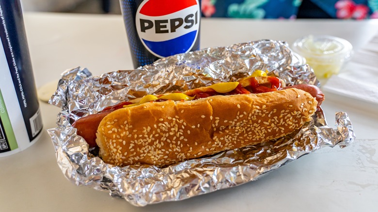 A Costco hot dog wrapped in foil with a Pepsi drink in the background