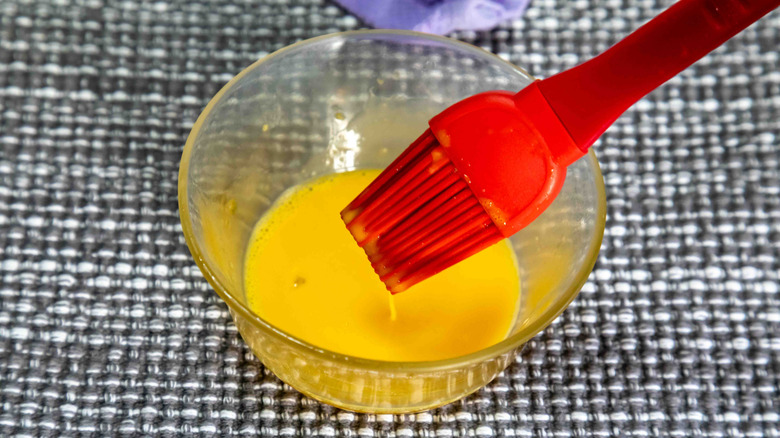 Egg wash in a glass ramekin with a silicone pastry brush