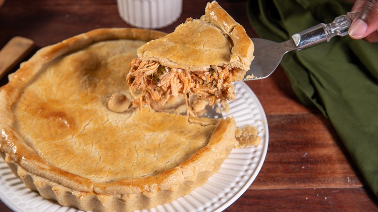 Slice of chicken pot pie being removed from a whole pie on a white plate
