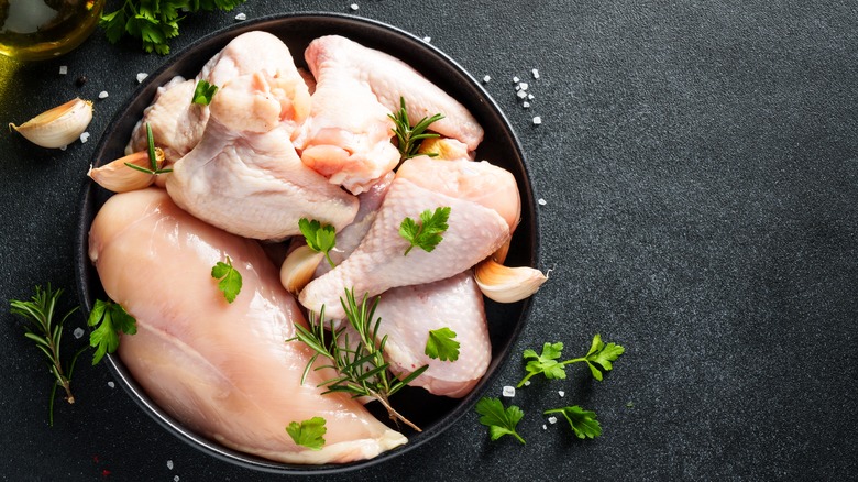 Black bowl filled with raw chicken pieces and garnished with fresh herbs