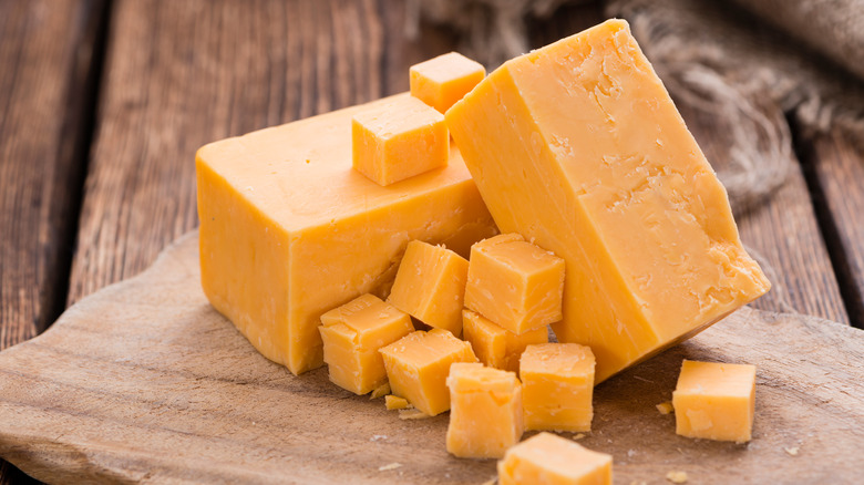 Cubes and blocks of orange cheddar cheese on a wooden board.