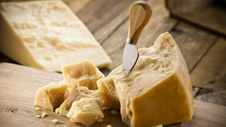 A hard, crumbly cheese cut with a knife on a wooden board.