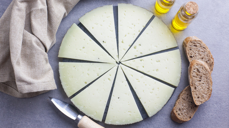 Manchego cheese slices positioned in a circle next to a knife, napkin, oil in bottles, and bread slices.