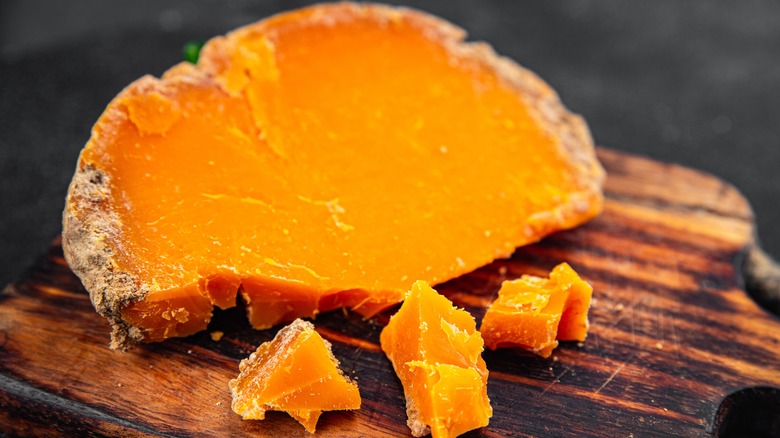 A wedge of Mimolette with some chunks next to it on a wooden board.