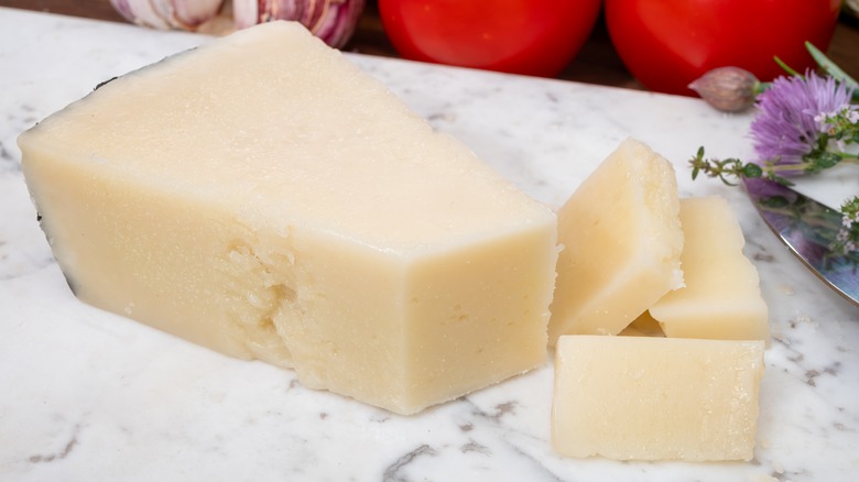 A wedge of pecorino cheese on a marble slate next to flowers and tomatoes.