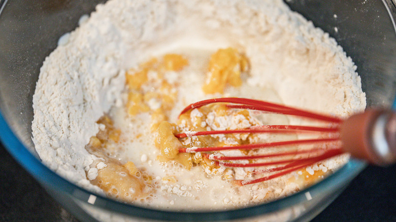 Using a whisk to stir eggs into flour and milk