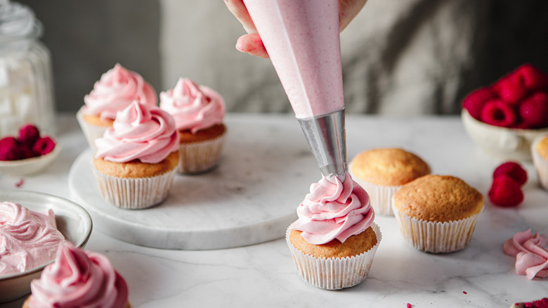 Person frosting cupcakes with a piping tip