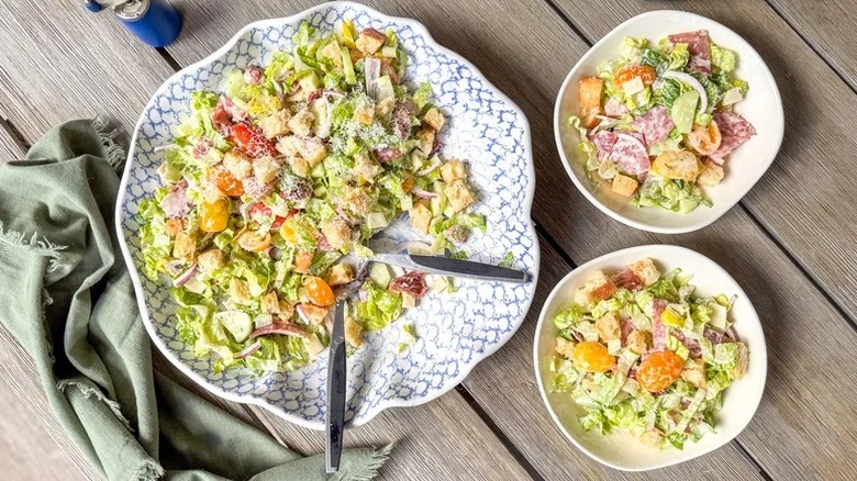 a large serving bowl and two smaller bowls of Italian Deli Grinder Salad on a wooden table