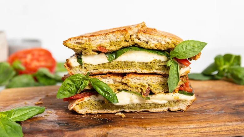 two halves of a Pesto Caprese Panini stacked on a wooden cutting board